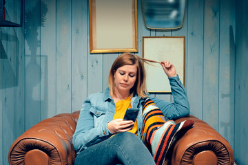young blond woman stretching hair and sitting on a vintage leather armchair is engrossed in her...