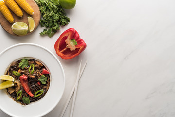 top view of delicious spicy thai noodles near chopsticks, corn. bell pepper, and parsley on marble grey surface