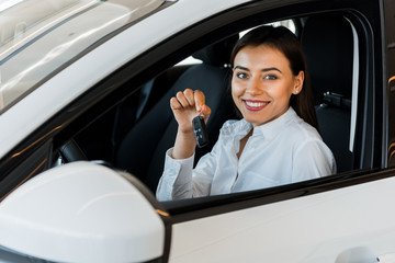 selective focus of happy woman holding car key while sitting in car