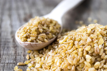 Dry bulgur grain in a wooden spoon. Healthy, dietary, vegan, gluten free product.
