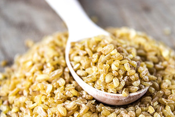 Dry bulgur grain in a wooden spoon. Healthy, dietary, vegan, gluten free product.