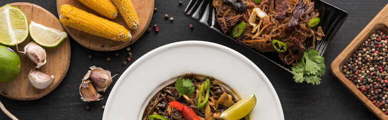 top view of tasty spicy thai noodles near chopsticks and fresh ingredients on wooden grey surface, panoramic shot