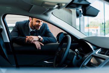 selective focus of cheerful bearded man looking at modern car