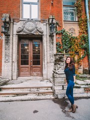 Obraz na płótnie Canvas Brunette girl with long hair in a shirt costs near the ancient beautiful doors on the wall colorful autumn ivy