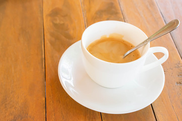 Hot coffee in a white cup with saucer on a wooden table.
