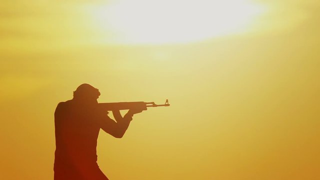 Islamic warrior with Kalashnikov at sunset day. Muslim fighter is training with a machine gun at sunset.
