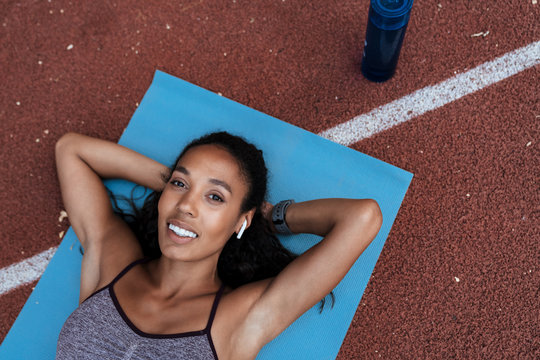 Image of african american woman with earpods lying on mat outdoors