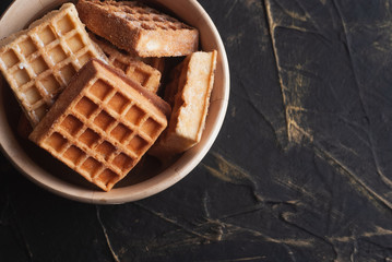 Delicious waffles in a wooden bowl, on a black background, flat lay,