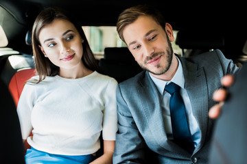 selective focus of cheerful woman and man in suit sitting in car