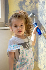 Fototapeta premium Little kid girl paints wall by paint roller