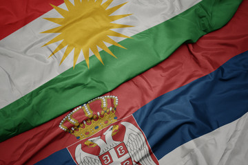 waving colorful flag of serbia and national flag of kurdistan.