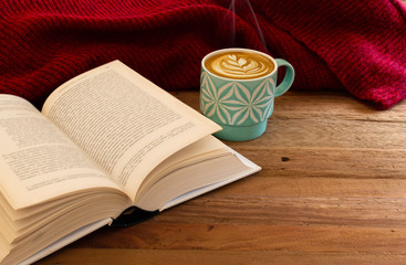 Still life details, cup of latte or cappuccino coffee with a book and red sweater on a wooden table.