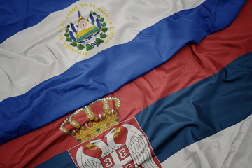 waving colorful flag of serbia and national flag of el salvador.