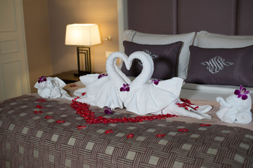 two swans made from towels are kissing on honeymoon white bed