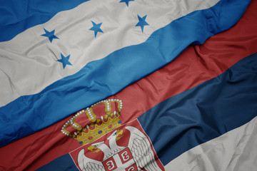waving colorful flag of serbia and national flag of honduras.