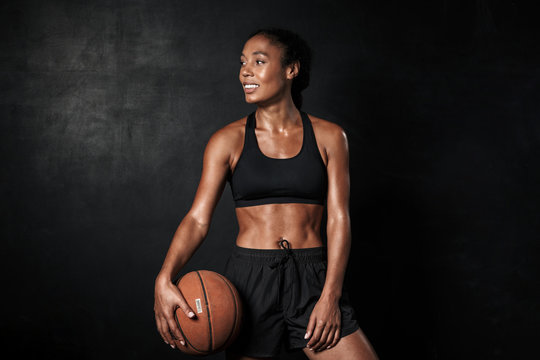 Image of smiling african american woman in sportswear holding basketball