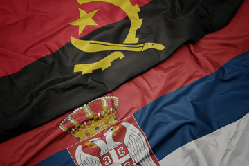 waving colorful flag of serbia and national flag of angola.