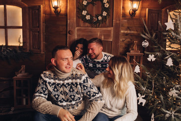 Naklejka na ściany i meble Two married couples are friends. Together celebrate the New Year. Celebrate Christmas. Champagne in the hands of girls and boys. Against the background of a wooden house. Cozy atmosphere