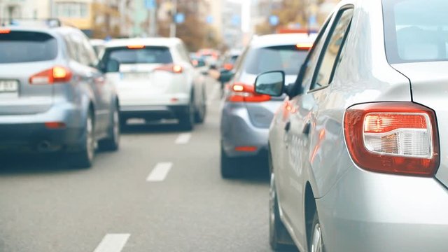 Cityscape of city road with car traffic jam with close-up vehicle rear stop lights during rush hour time. Many vehicles moving slow on street