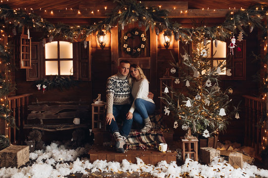 Christmas portrait of a romantic couple. Guy hugs the girl and kisses. They sit in a beautiful house. Christmas mood of lovers on the background of decorative snow and flying serpentine. Studio photo