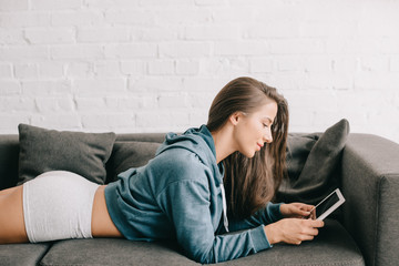beautiful woman in panties using digital tablet while lying on sofa