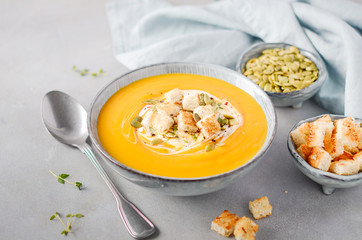 Pumpkin soup with cream, croutons, pumpkin seeds and thyme on a gray concrete or stone background.