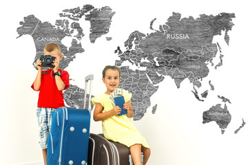 Adorable kids brther and sisterwith a suitcase sitting world map