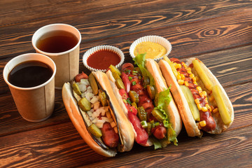Three hot dogs with yellow mustard and ketchup on a wooden table. Business lunch with tea and coffee