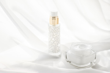 Face cream moisturizer jar and serum gel on white silk, skin care lotion and lifting emulsion,...