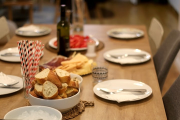Table set for dinner party with plates, bread, ice, paper straws and spread. Selective focus.