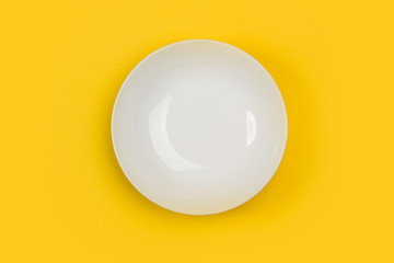 Plato blanco redondo sobre fondo amarillo liso y aislado. Vista superior. Copy space
