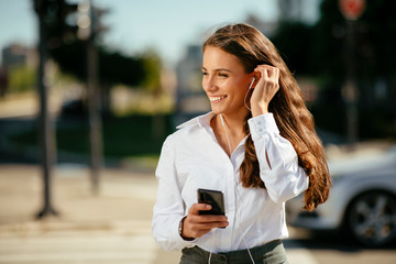 Young businesswoman using phone and listening music outside