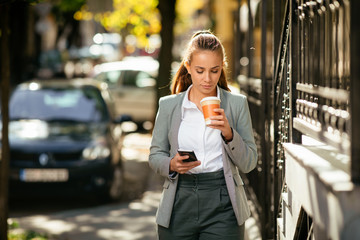 Young woman in city using phone on coffee break