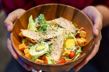 Healthy vegetable salad in a brown wooden cup with holding hand.