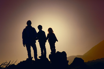 Fototapeta na wymiar Father with kids-boy and girl- travel in sunset mountains