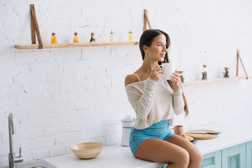happy young woman holding cup of coffee in kitchen