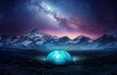 Tuinposter Kamperen in de bergen onder de sterren. Een tent opgezet en gloeiend onder de melkweg. Foto composiet. © James Thew