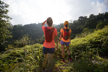 Fototapeta na wymiar Two women trail runners looking at the sunrise landscape after running to the top of tropical forest moutain