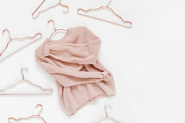 Pale pink knitted sweater with metallic hangers on white background. Autumn and winter clothes....