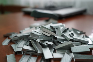 Many clips for a stapler on a wooden table. Stapler with a bunch of paper clips on the table.