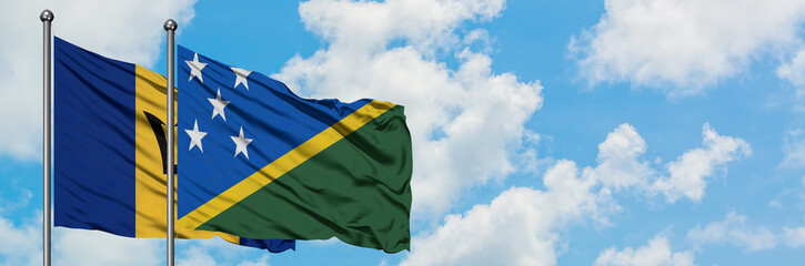 Barbados and Solomon Islands flag waving in the wind against white cloudy blue sky together. Diplomacy concept, international relations.