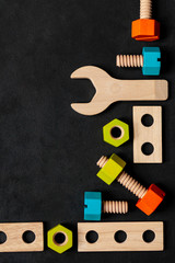 Set of colorful children's wooden toys. Construction kit with nuts and screws on dark black background. Interesting and fun game for boys and adults. Flat lay, top view, copy space for text