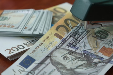 Fototapeta premium The stapler fastens the dollar and euro notes with iron clips. Stapler with paper clips on the background of banknotes.