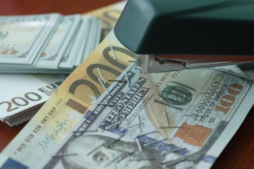 The stapler fastens the dollar and euro notes with iron clips. Stapler with paper clips on the background of banknotes.
