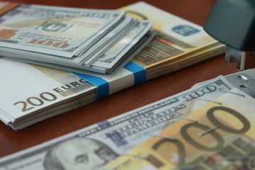The stapler fastens the dollar and euro notes with iron clips. Stapler with paper clips on the background of banknotes.