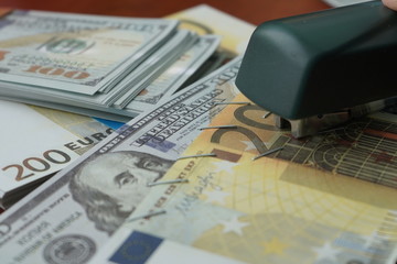 The stapler fastens the dollar and euro notes with iron clips. Stapler with paper clips on the background of banknotes.