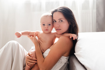 Mother and her baby son lying in bed on white sheets. Top view.