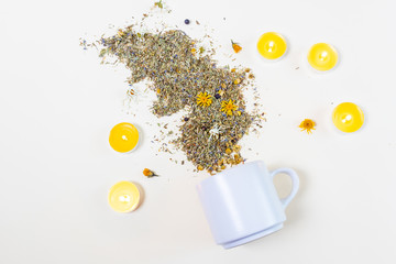 Fototapeta na wymiar White cup lies on a light background. Candles are standing nearby. Around scattered dry healing grass and flowers. The concept of healthy tea, a natural cold medicine. Minimalism.