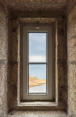 view of the ocean through a lighthouse window in the stone staircase