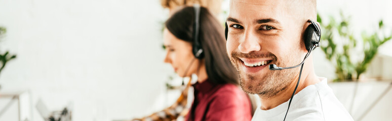panoramic shot of cheerful broker in headset working in office with coworkers
